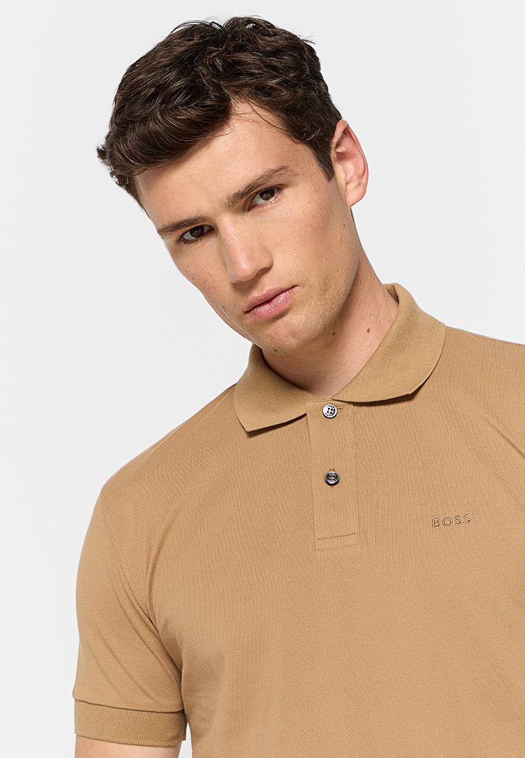 Polo marron avec un tissu texturé, patte de boutonnage à deux boutons et logo discret. Manches courtes et design de col classique.