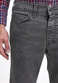 Šedé džínové džíny s běžným střihem, standardním designem s pěti kapsami, kontrastním prošitím a hladkou texturou.