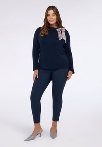 Maglione lavorato a maglia blu navy con dettaglio a fiocco sulla spalla, abbinato a pantaloni slim fit blu navy e décolleté grigio chiaro.