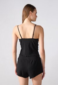 Čierny rebrovaný bezrukávový top so scalloped lemom, kombinovaný s šortkami, so priliehavým strihom a ľahkým materiálom. Jednoduchý a minimalistický štýl.