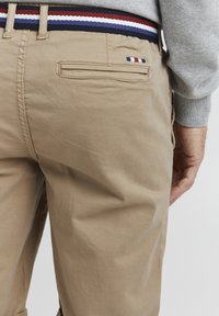 Khaki bukser med tekstureret finish, der har en baglomme og en flerfarvet talje i rød, hvid og blå.