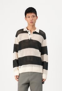 Pull-over en tricot avec un col, présentant un design en maille avec des rayures blanches et noires alternées. Poignets et ourlet côtelés.