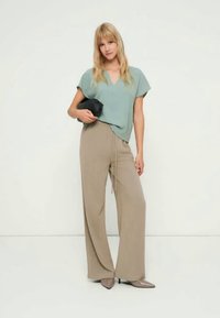 Világoskék rövid ujjú felső bézs, magasderekú, széles szárú nadrággal párosítva. A modell egy fekete táskát tart a kezében. Semleges színű cipő teszi teljessé a szettet.