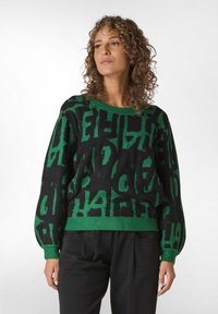 Svart tröja med gröna abstrakta bokstäver. Har en rund halsringning, långa ärmar samt ribbade mudd och nederkant. Mjuk textur.