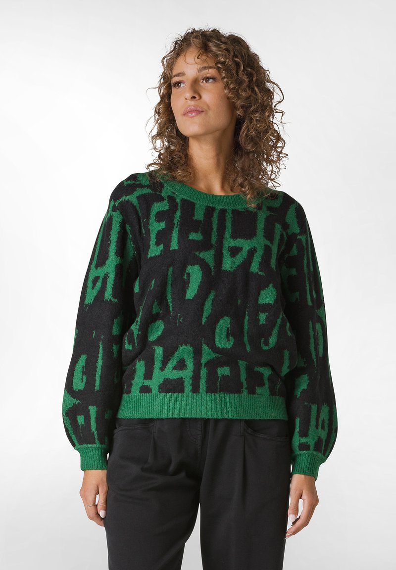 Svart tröja med gröna abstrakta bokstäver. Har en rund halsringning, långa ärmar samt ribbade mudd och nederkant. Mjuk textur.