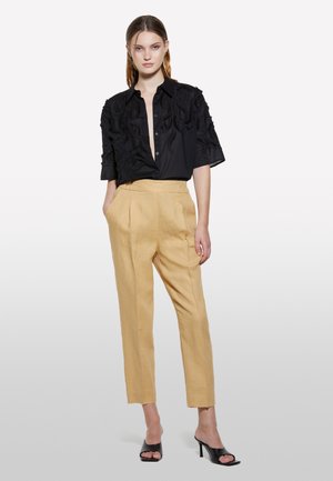 Chemise noire avec des détails texturés et des manches courtes, associée à un pantalon beige clair ajusté et des talons ouverts noirs.