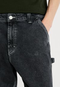 Jeans de denim negro con un corte recto clásico, cierre de botón plateado, costuras blancas en contraste y detalle de bolsillos laterales.