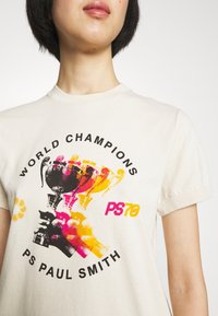 Camiseta de algodón color crema con un estampado gráfico de trofeos coloridos y el texto "CAMPEONES DEL MUNDO" y "PS PAUL SMITH". Mangas cortas.