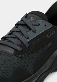 Close-up de um sneaker Clarks preto e cinza escuro com tecido texturizado, atacadores grossos e detalhes cosidos na lateral e na sola.