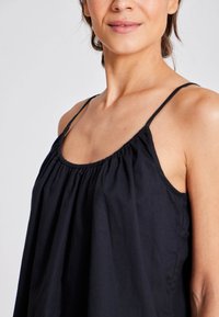 Top negru fără mâneci, cu gât strâns și bretele subțiri. Material ușor și design fluid. Fără modele sau accesorii vizibile.