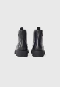 Bottines en cuir noir avec une semelle en caoutchouc noir robuste et des languettes à l'arrière. Surface lisse et design minimaliste.