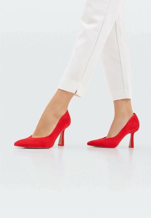 Rote Wildleder-Hochzeitsschuhe mit spitzem Zehenbereich und V-förmigem Ausschnitt, ausgestattet mit einem schlanken Absatz und glatter Textur, vor hellem Hintergrund.