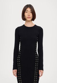 Black ribbed knit dress features long sleeves, round neckline, and lacing with gold eyelets along the sides for detailed accentuating.
