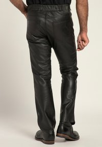Schwarze Lederhosen mit schickem Design, ausgestattet mit Gesäßtaschen und einer glatten Textur. Von hinten mit dunklem Schuhwerk präsentiert.
