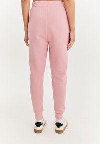 Svetloružové tepláky vyrobené z mäkkého materiálu, s elastickým pásom, zúženými nohavicami a rebrovanými manžetami. Nosené s bielymi teniskami.