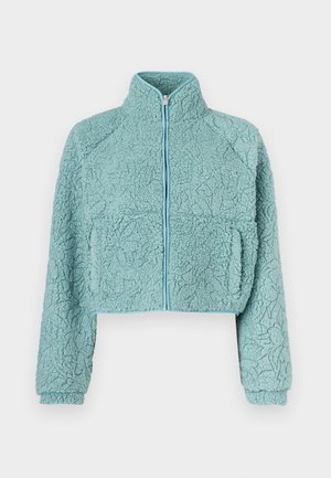 Chaqueta recortada con cremallera en material suave y texturizado azul claro; cuenta con mangas raglán y dos bolsillos delanteros con ribete en contraste.