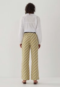 Vit långärmad skjorta i kombination med gröna och vita byxor med vågmönster och vida ben, som har elastiskt midjeband och klackskor med blockklack.