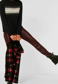 Black sweater with a cream and gray patterned yoke, paired with burgundy faux leather pants. Holding a black and red checkered outer layer.