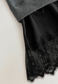Grå strikket top dækker en sort satin nederdel, der har en delikat sort blondekant med indviklede blomster broderier og frynser.