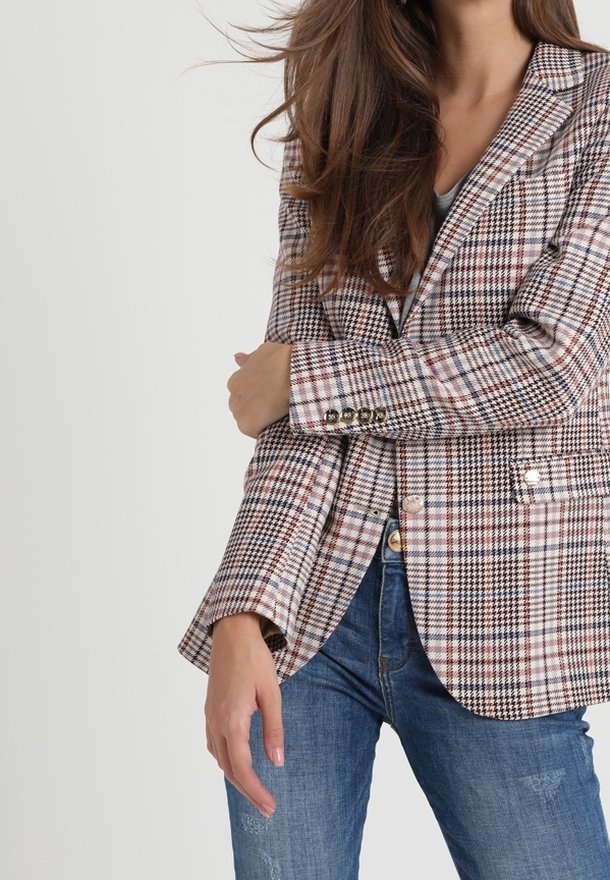 Blazer à carreaux beige, noir et bordeaux. Présente une coupe ajustée, des boutons décoratifs et des revers à encoche. Associé à un jean bleu.