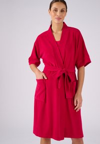 Fuchsia badjas gemaakt van zacht materiaal. Heeft een riem, korte mouwen en twee voorkruiken. Gladde textuur en knielange ontwerp.