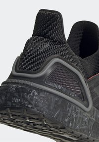 Gros plan sur le talon d'une chaussure de sport noire avec tissu tricoté texturé, marquage "007" et semelle noire matelassée à motifs.