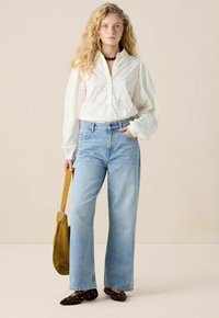 White blouse with textured embroidery, light blue high-waisted jeans, brown suede pointed-toe flats, and a tan shoulder bag.