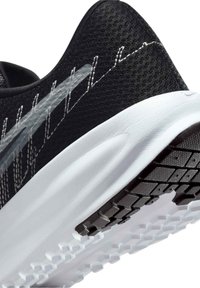 Gros plan du talon d'une chaussure de course noire avec semelle blanche amortissante et motif de semelle texturé noir et blanc.