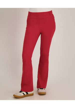 Rode rechte broek gedragen met witte sneakers met zwarte strepen en rubberen zolen, getoond van taille tot voeten op een neutrale achtergrond.