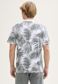 Camiseta blanca con un patrón de hojas de palma en negro y gris, escote redondo, mangas cortas y corte relajado. Tejido de algodón con una textura suave.