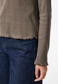 Top lungo a maniche ribatte con scollatura a onde, tessuto texturizzato e maniche fitted, abbinato a jeans blu scuro.