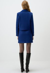 Blue textured jacket with matching skirt. Features a notched collar and silver-button accents on sleeves. Black knee-high boots complete the look.