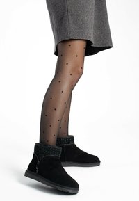 Botas de tobillo de ante negro con puños texturizados y con cuentas, y suela plana, combinadas con medias negras semitransparentes con lunares.