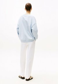 Felpa oversize azzurro chiaro, pantaloni bianchi a gamba dritta e sandali neri con dettagli dorati. Texture lisce e morbide, design minimalista.