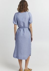 Světle modré lněné šaty s krátkými nabíranými rukávy, zavázaným pasem a délkou po kolena. Obsahují detail bočních knoflíků a mírnou texturu.