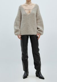 Beige gestrickter Pullover mit tiefem V-Ausschnitt und übergroßen Ärmeln, kombiniert mit eleganten schwarzen Lederhosen und Absatzstiefeletten.