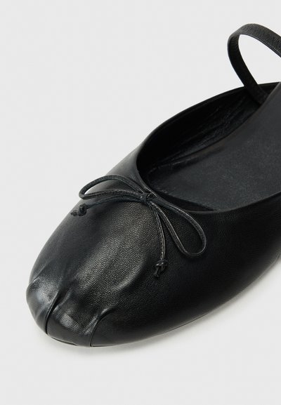 Black leather ballet flats feature a rounded toe, a small bow detail at the front, and a flat sole. Texture is smooth with a subtle sheen.