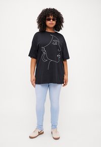 Svart oversized t-skjorte med hvit abstrakt ansikt-linje tegning, kombinert med lyseblå jeans og beige sneakers, med en avslappet passform og korte ermer.