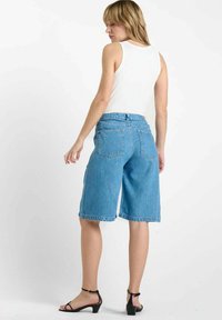Blauwe denim shorts met een losse pasvorm, knielange zoom en vijf-pocket ontwerp. Gemaakt met een aangesloten witte tanktop en zwarte sandalen.