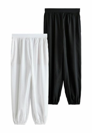 Femme portant une veste bomber bordeaux, un pantalon noir à jambes larges, un crop top rayé et des ballerines noires, debout devant un fond neutre.