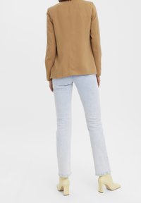 Blazer marron ajusté, jean en denim bleu clair et chaussures à talons blocs jaunes. Le tissu est lisse avec une coupe structurée, présentant peu de détails.