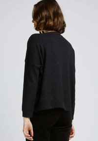 Un pull noir surdimensionné en tissu doux. Présente un col en scoop et un ourlet côtelé. Inclut un dos légèrement plus long.
