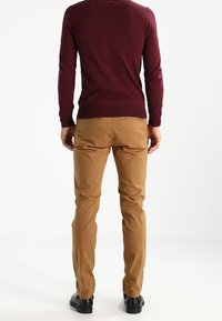 Bordeaux gebreide trui en tan chino's, met een getailleerde pasvorm. De chino's hebben een gladde textuur, zakdetails en vallen net boven de schoenen.