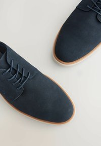 Scarpe in tessuto blu navy con upper in texture, design con lacci e suole in gomma marrone chiaro. Punta arrotondata e stile minimalista.