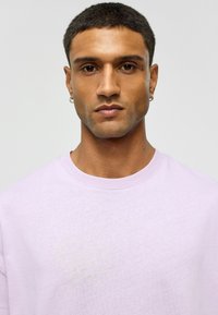 Lichtpaarse crewneck t-shirt met een zachte textuur. Heeft korte mouwen en een ontspannen pasvorm, weergegeven tegen een effen achtergrond.