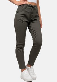 Dunkelgrüne, schmal geschnittene Hose mit hoher Taille, Knopfverschluss, Seitentaschen und strukturiertem Stoff, kombiniert mit weißen Sneakers.