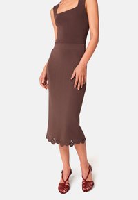 Robe en tricot marron avec un décolleté carré, un corsage ajusté et un ourlet festonné avec des découpes florales. Assortie à des sandales rouges à lanières.