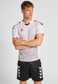 Hvid fodboldtrøje med kortærmer og bikage-mønster samt sorte detaljer, kombineret med sorte shorts med hvide chevron-striber.