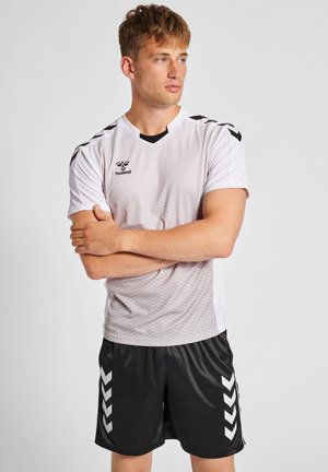 Witte voetbalshirt met korte mouwen, voorzien van een honingraatpatroon en zwarte accenten, gecombineerd met zwarte shorts met witte chevronstrepen.