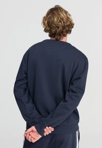 Felpa blu navy con maniche lunghe, colletto tondo e polsini e orlo a costine. Texture liscia, presenta una vestibilità comoda e nessuna grafica visibile.